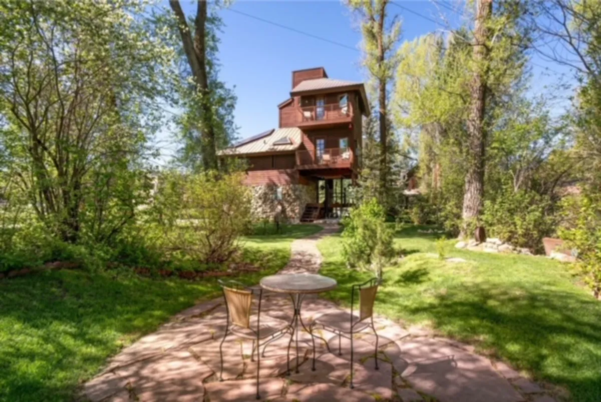 This image captures a tranquil garden seating area just outside the house, featuring a pathway that leads to the entrance and is surrounded by trees and lush landscaping. The space looks ideal for morning coffee, picnics, or family gatherings outdoors.