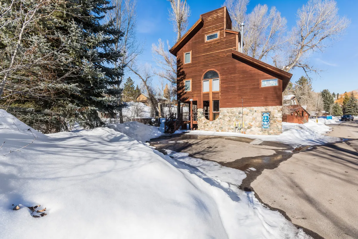 A striking view of the house’s unique architectural design, set against a backdrop of snow-covered ground and surrounded by trees, capturing the wintry mountain town ambiance. The tranquil setting hints at easy access to winter sports and the peaceful cul-de-sac location described in the text.