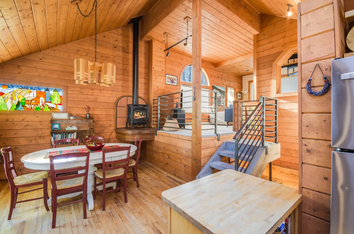 This image features the main gathering area inside Soda Creek Haus, showing a dining table set near a striking stained glass window, a cozy fireplace, and a glimpse of the staircase. The interplay of warm natural light and decorative glass brings a unique vibrancy to the space, perfectly capturing the spirit described in the section.