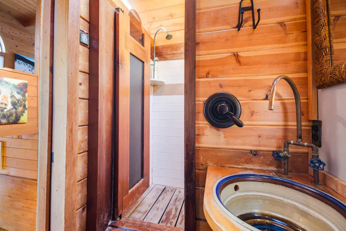 A close-up of the main floor's rustic walk-in shower, featuring wood-paneled walls, a ceramic sink, and a rain-style showerhead. The space exudes warmth and craftsmanship, offering an architecturally distinct touch that makes the bathroom a memorable part of the main floor experience.